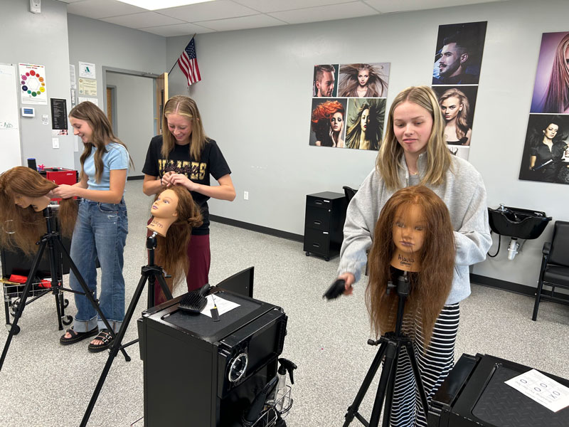 3 women working on cosmetology mannequin heads